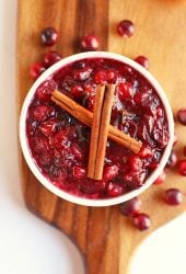 Finished cranberry sauce in a white bowl with two cinnamon sticks